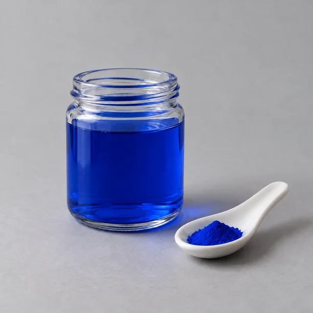 A small glass jar of water colored by Blue 2 dye, with dry dye powder on a spoon