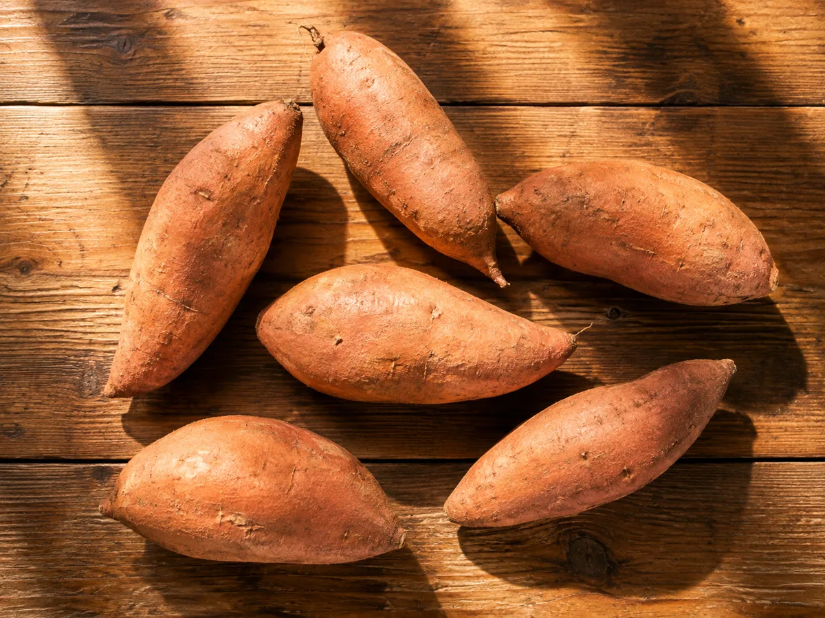 Whole fresh sweet potatoes on a wooden surface for a blood-pressure-friendly food guide.